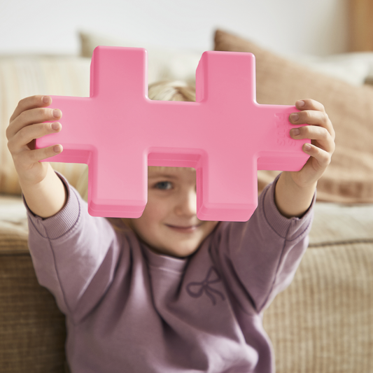 KÆMPE - Pastel Pink: a child holding a giant pastel pink Plus-Plus piece above their head