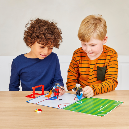 Learn To Build - Sports: two boys playing with Plus-Plus hockey players on a play mat