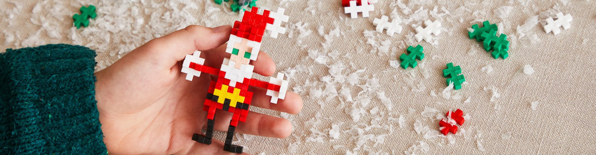 Hand holding a Plus-Plus Santa build over snow with scattered red and green pieces