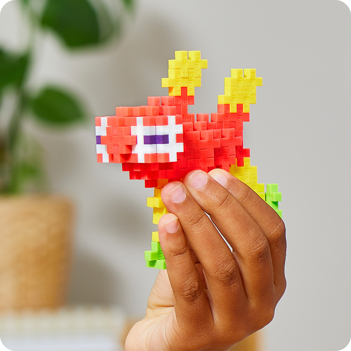 Built with just one shape: hand holding a red and yellow Plus-Plus axolotl build