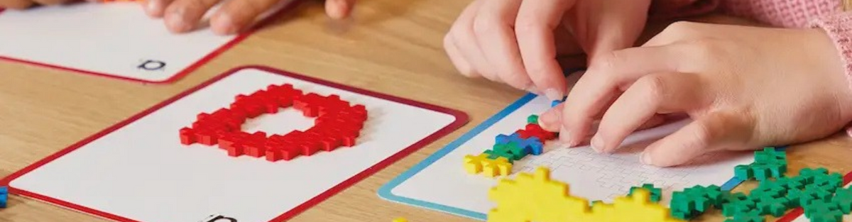 Children's hands building red and yellow Plus-Plus shapes on classroom pattern cards