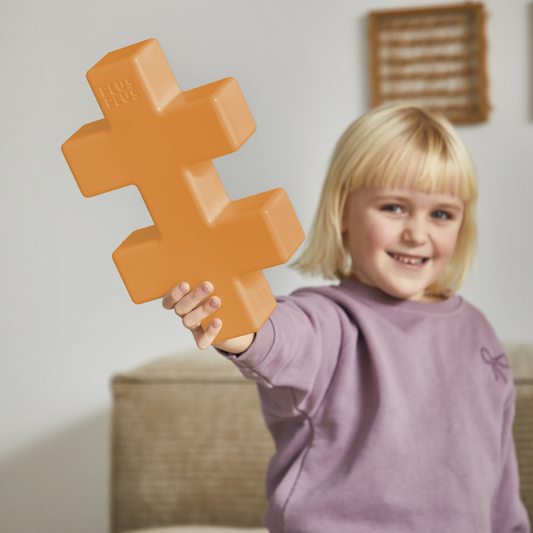 KÆMPE - Orange: a smiling child holding up a giant orange Plus-Plus piece