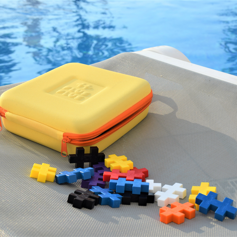 Yellow Plus-Plus travel case and colorful pieces by a pool