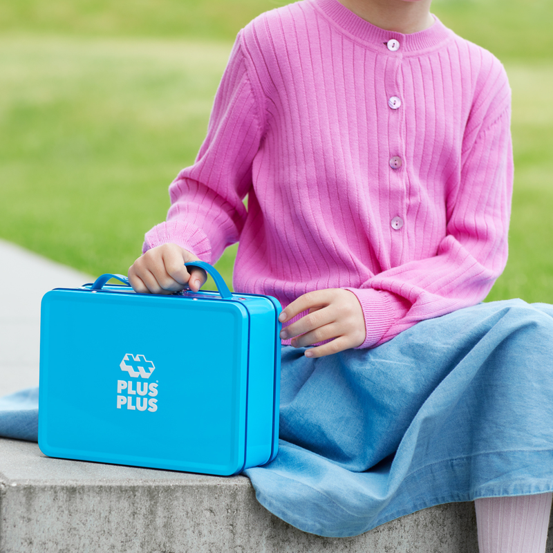 Girl in a pink sweater holding a blue Plus-Plus travel case outdoors